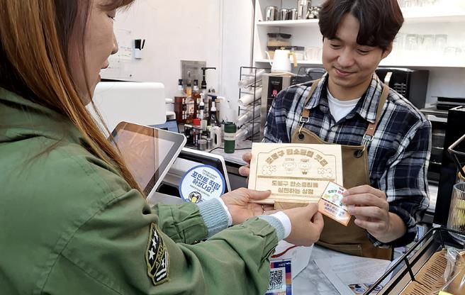 구 직원이 탄소중립 맛집 가게에 안내판을 전달하고 있다.